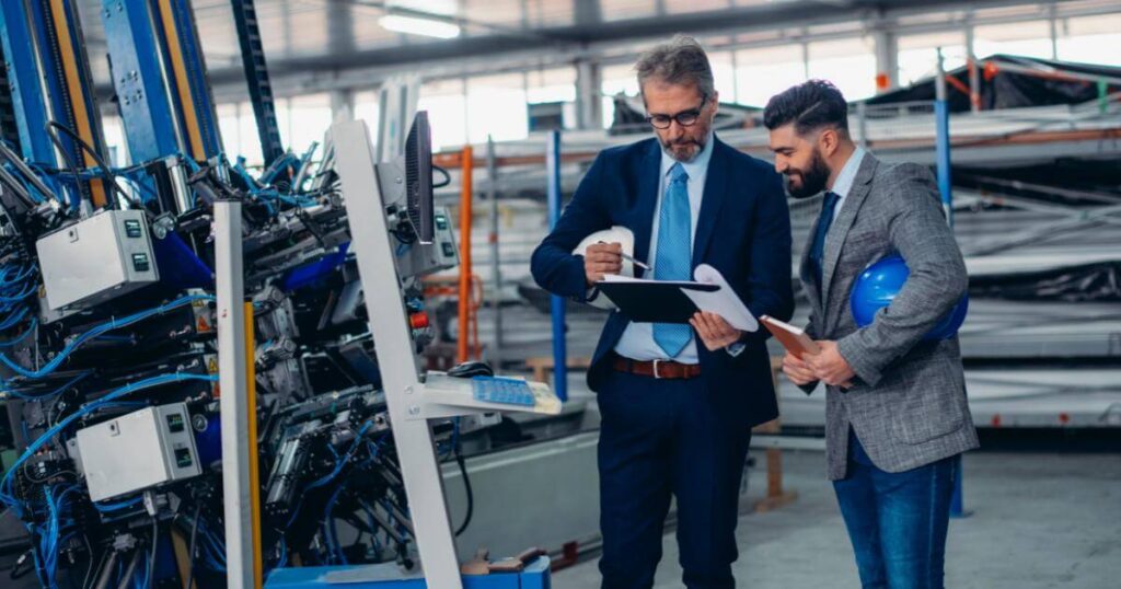 two manufacturing leaders on shop floor looking at clipboard with pleased look
