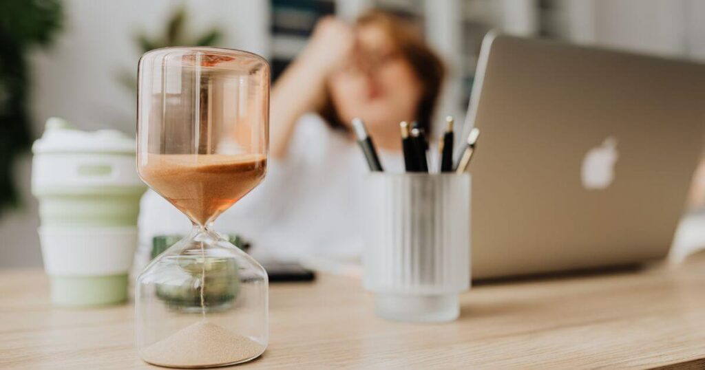 hourglass on office desk with stressed employee in the background