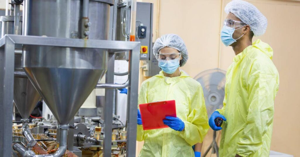 Two food manufacturing workers in protective gear reviewing a clipboard on the production floor