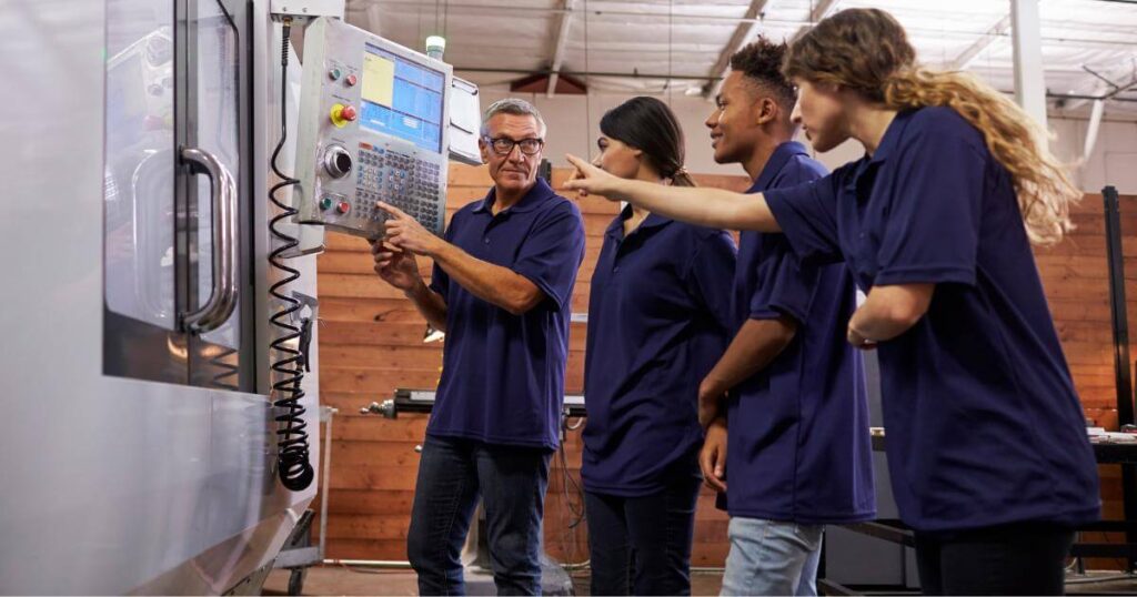 Experienced manufacturing employee training three new workers on CNC machine controls on the production floor